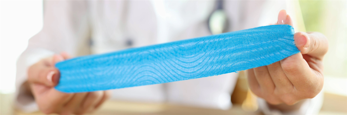 Ergotherapeutin legt Kinesio-Tape am Handgelenk und an den Fingern einer Patientin in der Handrehabilitation an