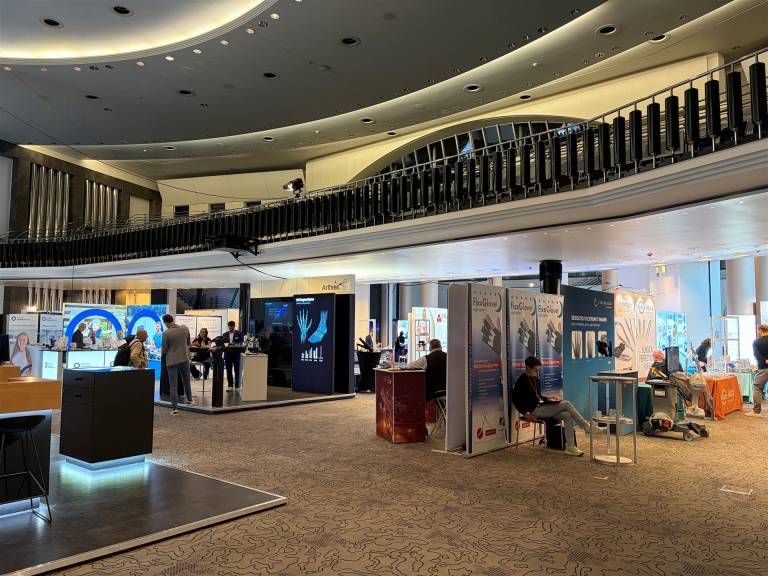 Innenansicht einer geräumigen Messehalle mit verschiedenen Ausstellungsständen und Besuchern.